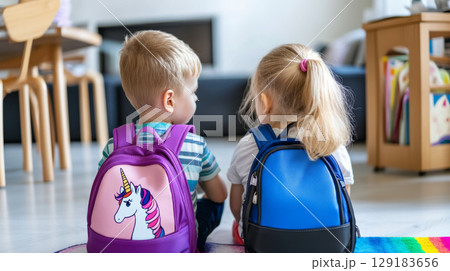 Two children with school backpacks sitting indoors, viewed from behind Two children with school backpacks sitting indoors, viewed from behind 129183656