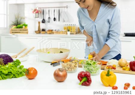 Young Woman Cooking in the kitchen. Healthy Food - Vegetable Salad Diet. Healthy Lifestyle. Cooking delicious food during the COVID-19 self-quarantine 14 days. Stay at home concept. 129183961