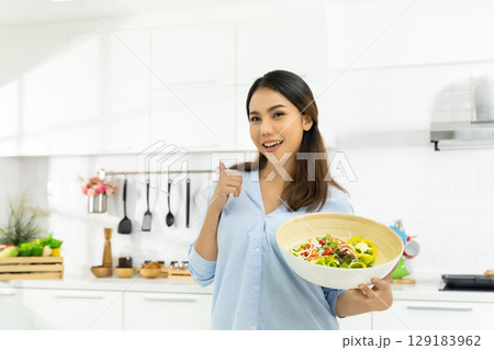 Young Woman Cooking in the kitchen. Healthy Food - Vegetable Salad Diet. Healthy Lifestyle. Cooking delicious food during the COVID-19 self-quarantine 14 days. Stay at home concept. 129183962