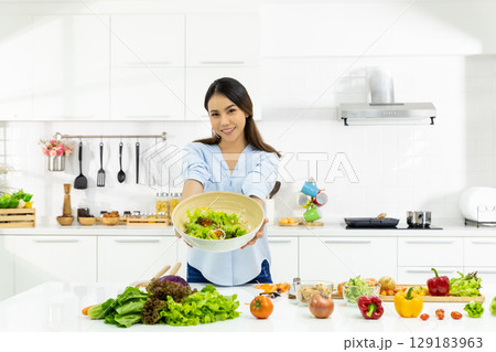 Young Woman Cooking in the kitchen. Healthy Food - Vegetable Salad Diet. Healthy Lifestyle. Cooking delicious food during the COVID-19 self-quarantine 14 days. Stay at home concept. 129183963