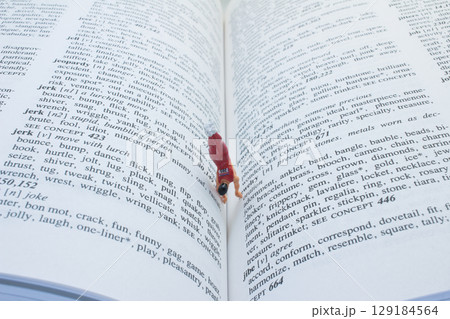 Miniature Figure Climbing the Pages of an Open Dictionary 129184564