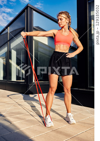 Athletic Woman Exercising with Resistance Band on a Sunny Rooftop Athletic Woman Exercising with Resistance Band on a Sunny Rooftop 129185032