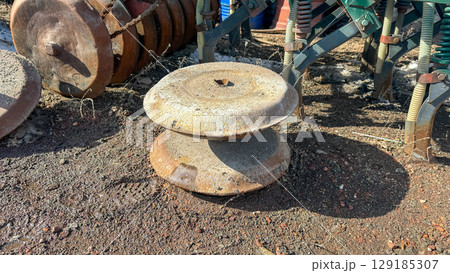 Close-up of old, rusty agricultural disc blades on soil, part of a vintage farm machine, symbolizing forgotten labor or rural history. Close-up of old, rusty agricultural disc blades on soil, part of a vintage farm machine, symbolizing forgotten labor or rural history. 129185307