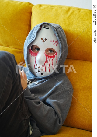 Child in Halloween Mask Relaxing on Yellow Couch Child in Halloween Mask Relaxing on Yellow Couch 129185344