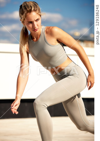 Female athlete in activewear exercising outdoors under the bright blue sky 129186248