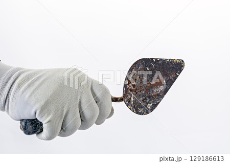 Hand in white rubber glove holds rusty metal trowel against plain background, suggesting focus on gardening or construction tools Hand in white rubber glove holds rusty metal trowel against plain background, suggesting focus on gardening or construction tools 129186613