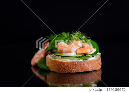 Small canapes with shrimps, salad and cucumbers on a black background Small canapes with shrimps, salad and cucumbers on a black background 129186672