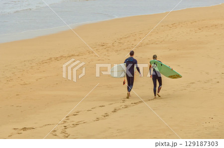 surfers strolling along the beach surfers strolling along the beach 129187303