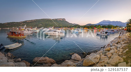 Moonlight beach at dusk in Kemer resort, Turkey. Calis hill and majestic Taurus mountains with Olympos peak Tahtali in the background. Lively atmosphere at the bay with boats illuminating the water Moonlight beach at dusk in Kemer resort, Turkey. Calis hill and majestic Taurus mountains with Olympos peak Tahtali in the background. Lively atmosphere at the bay with boats illuminating the water 129187537