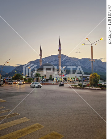 KEMER, TURKEY - JULY 1, 2025 Evening scene in Kemer featuring the grand mosque Huzur Camii Dzamija with two minarets and dome, and Taurus mountains at horizon. Active city life with street traffic KEMER, TURKEY - JULY 1, 2025 Evening scene in Kemer featuring the grand mosque Huzur Camii Dzamija with two minarets and dome, and Taurus mountains at horizon. Active city life with street traffic 129187547