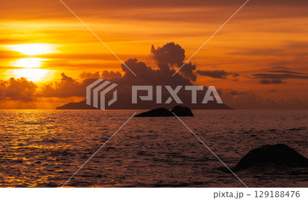 Golden Sunset Over Ocean with Island and Clouds in the Distance Golden Sunset Over Ocean with Island and Clouds in the Distance 129188476