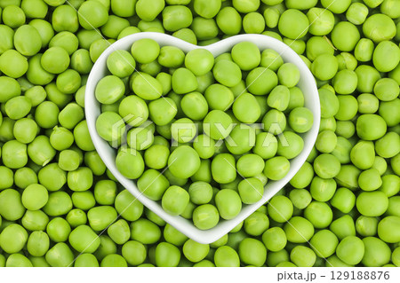 Fresh green peas in white ceramic bowl as a background. Top view. Flat lay Fresh green peas in white ceramic bowl as a background. Top view. Flat lay 129188876