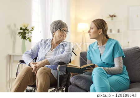 Doctor Or Nurse Reading Book With Senior Patient In Wheelchair Doctor Or Nurse Reading Book With Senior Patient In Wheelchair 129189543