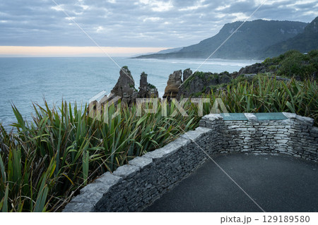 Empty viewpoint overlooking rugged coastline and ocean during sunset, New Zealand 129189580