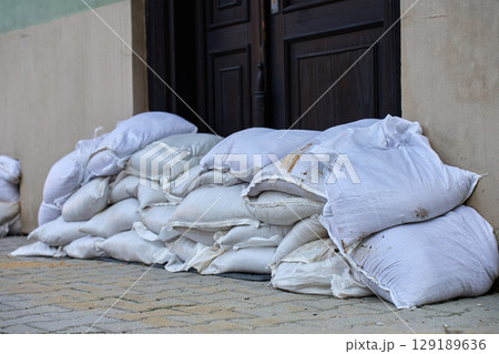 Sandbags stacked in front of door to protect building from flood water. Emergency defense measure against storm damage and natural disaster in urban residential area 129189636