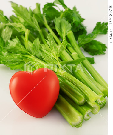 Healthy food concept. Green celery with red heart on white background. Vegetarian and vegan diet. Greens are good for heart health 129189710