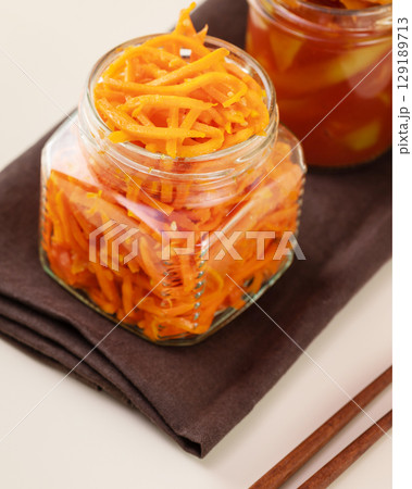 Probiotic food. Pickled or fermented vegetables. Korean carrot in glass jar on a brown napkin with chopsticks on a kitchen table. Home food preserving or canning. Close up Probiotic food. Pickled or fermented vegetables. Korean carrot in glass jar on a brown napkin with chopsticks on a kitchen table. Home food preserving or canning. Close up 129189713