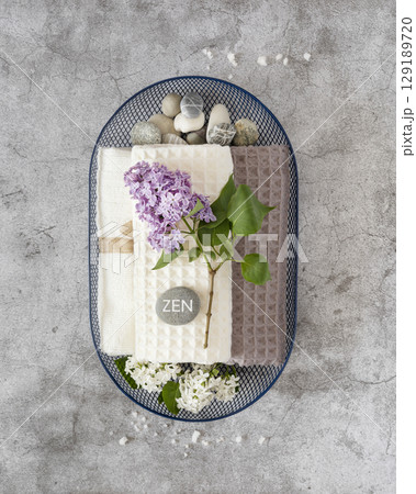 Wellness, Spa relax still life with massage stones with inscription Zen, towels and lilac flowers in a blue basket on a grey textured background. Self care and me time concept 129189720