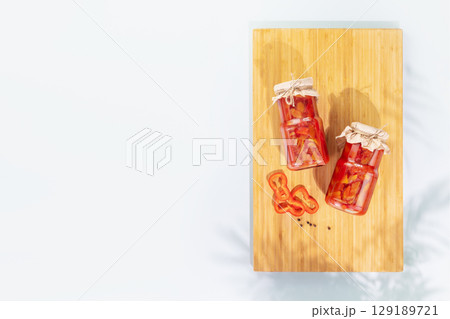 Probiotic food. Pickled or fermented vegetables. Lecho, sweet peppers in glass jars on a wooden board on a blue background with shadows and copy space. Mockup of food preserving or canning Probiotic food. Pickled or fermented vegetables. Lecho, sweet peppers in glass jars on a wooden board on a blue background with shadows and copy space. Mockup of food preserving or canning 129189721