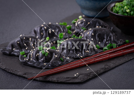 Japanese gyoza dumplings, made of black dough, black gyoza,with green onions and sauce, on a plate, close-up, 129189737