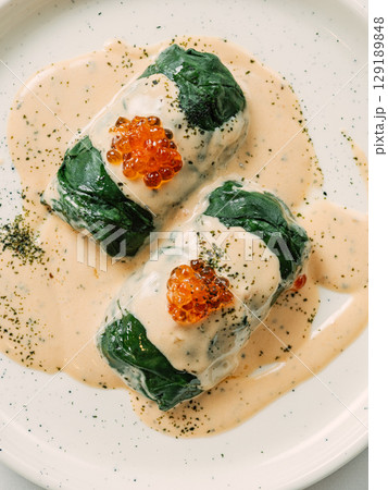 Stuffed green cabbage rolls with sauce in restaurant-style plating, served red caviar 129189848