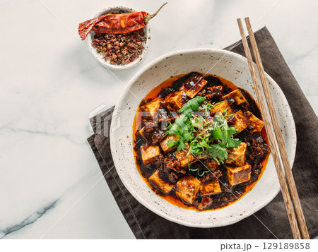 Spicy asian tofu salad or appetizer. Fried tofu decorated green onion - chinese dish with sauce. Serving Asian dish on white marble background. Top view, copy space 129189858