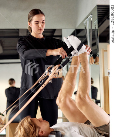 Fitness instructor guiding Pilates session with resistance straps in modern studio 129190083