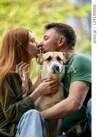 Couple sharing a moment with their dog outdoors in a loving embrace Couple sharing a moment with their dog outdoors in a loving embrace 129190088