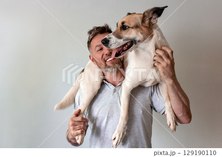 Man joyfully interacts with a dog perched on his shoulders indoors Man joyfully interacts with a dog perched on his shoulders indoors 129190110