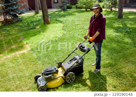 Man in backyard mowing lawn with yellow push mower on a sunny day 129190148