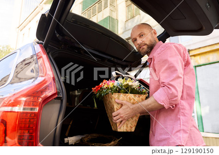 Man loading a flower basket into a car trunk outdoors 129190150