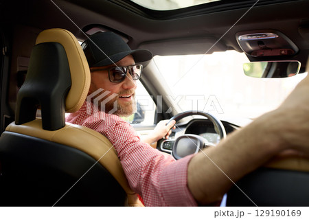 Smiling driver wearing a cap enjoying a sunny day inside a modern vehicle Smiling driver wearing a cap enjoying a sunny day inside a modern vehicle 129190169