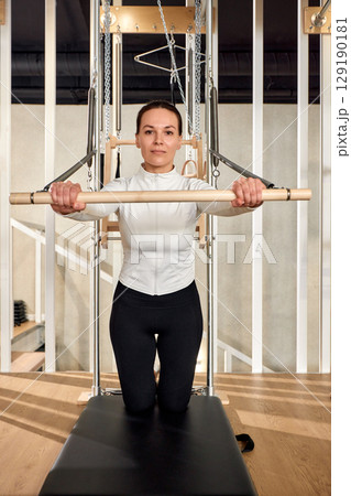Woman practicing pilates on a reformer machine in a fitness studio 129190181