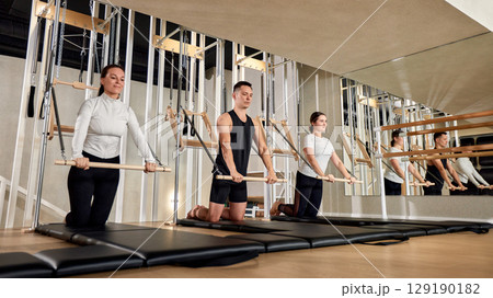 Group of individuals performing pilates exercises in a modern fitness studio Group of individuals performing pilates exercises in a modern fitness studio 129190182