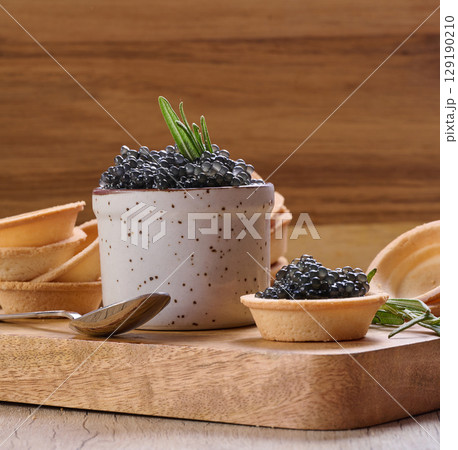 Black caviar in mini tartlet on wooden board, ceramic pot with caviar and stacks of empty tartlets.Wooden background Black caviar in mini tartlet on wooden board, ceramic pot with caviar and stacks of empty tartlets.Wooden background 129190210
