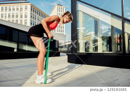 Young woman using a resistance band for a workout on a modern terrace 129191085