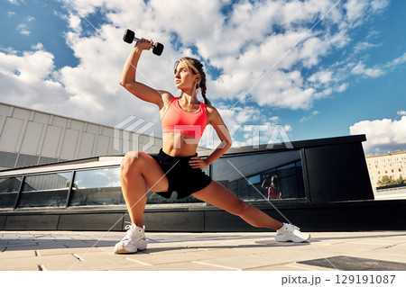 Woman exercising outdoors with dumbbell on a sunny day 129191087