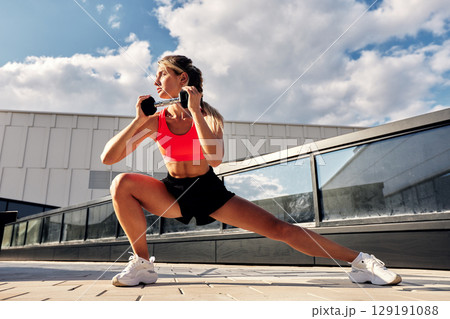 Woman performing fitness exercises with weights outdoors under a bright blue sky 129191088