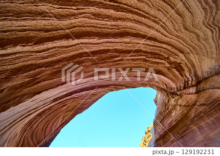 Sandstone Arch and Striated Rock Layers Framing Blue Sky Low Angle View 129192231