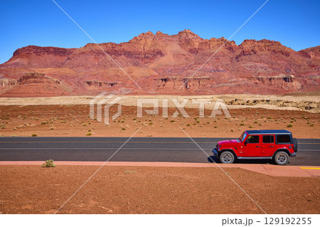 Red SUV on Desert Highway with Red Rock Formations Eye Level Perspective 129192255