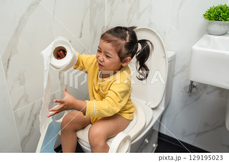 happy toddler girl is sitting on toilet with tissue at home. potty training and learning 129195023