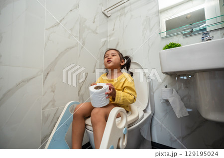 toddler girl sitting on toilet with tissue at home and suffering from stomachache and constipation toddler girl sitting on toilet with tissue at home and suffering from stomachache and constipation 129195024