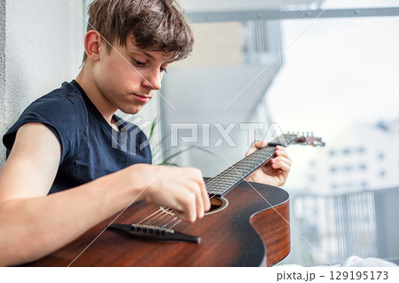 A teenager enthusiastically learns to play the guitar and tunes the strings in his free time while A teenager enthusiastically learns to play the guitar and tunes the strings in his free time while 129195173