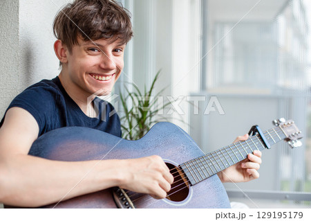 Cute cheerful teenage boy on balcony playing guitar, smiling at camera Cute cheerful teenage boy on balcony playing guitar, smiling at camera 129195179