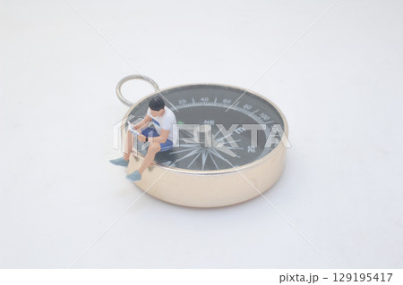 Miniature Person Sitting on a Compass Reading 129195417