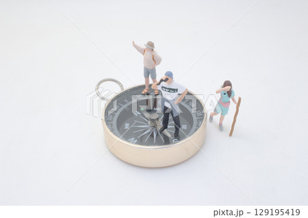 Miniature Explorers Standing on Compass Depicting Direction 129195419