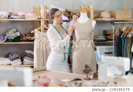 Woman tailor connects parts of dress on mannequin 129195574