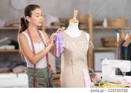 dressmaker works on a dress near a mannequin dressmaker works on a dress near a mannequin 129195588