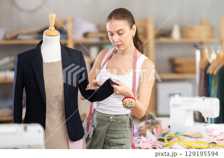 Young tailoress trying ready jacket on mannequin Young tailoress trying ready jacket on mannequin 129195594
