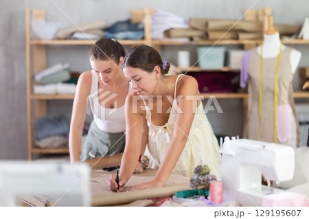 Two young female dressmakers drawing on paper Two young female dressmakers drawing on paper 129195607